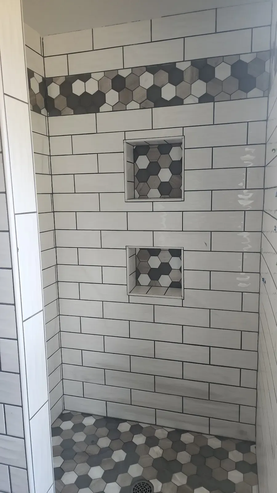 Subway tile walls, hex-accent niches, and hex floor tile during the cabin shower installation