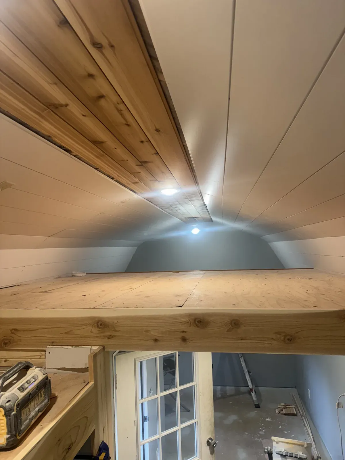 View from the loft across the finished vaulted ceiling with cedar accent planks, recessed lights, and an exposed beam