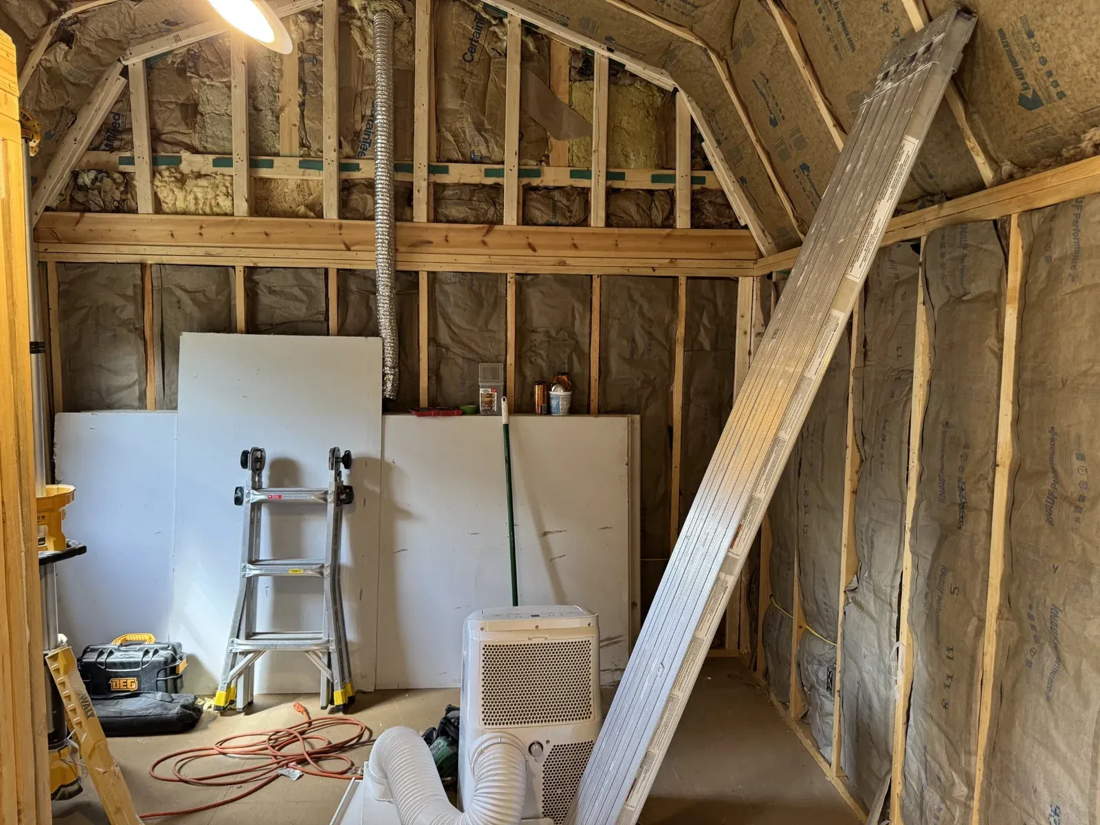 Shed interior framed and insulated, with drywall sheets stacked ready for installation