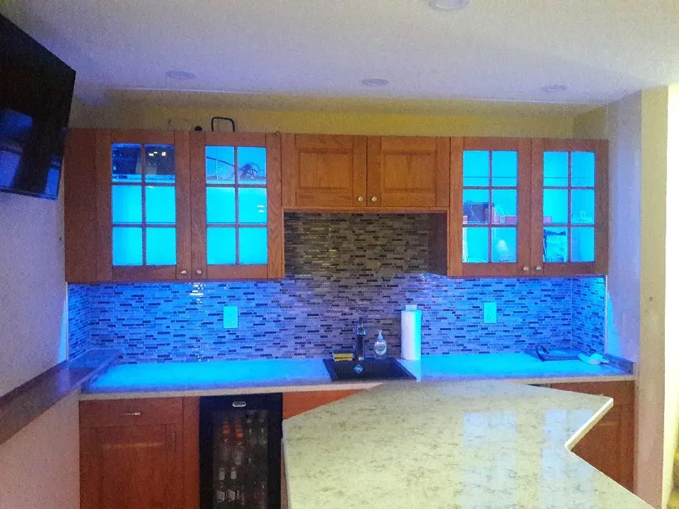 Finished basement wet bar with lighted glass-front cabinets and mosaic tile backsplash