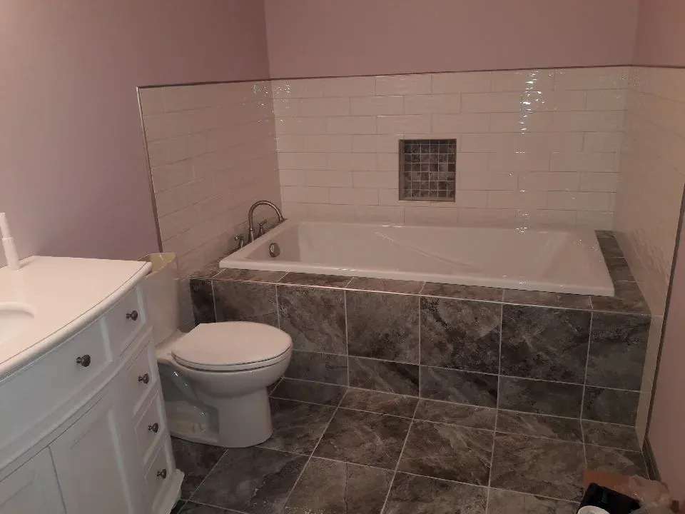 Finished basement bathroom with toilet, vanity, tiled floor, and tub surround