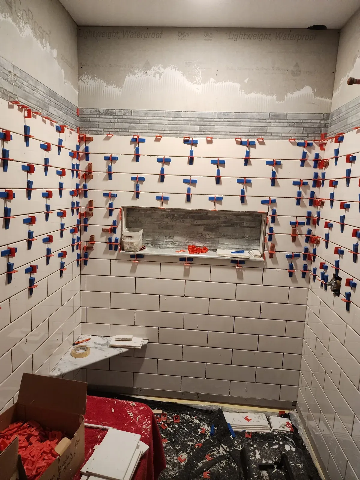 Subway tile, mosaic accent band, recessed niche, and marble corner bench during installation